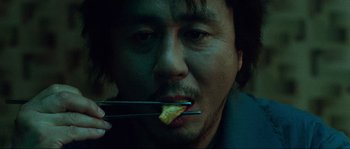 Movie still from “Oldboy” (2003), directed by Park Chan-wook – A man holding a fork in his mouth while eating something; Extreme Close Up shot, Overhead angle
