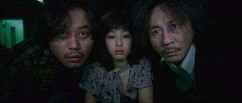 Movie still from “Oldboy” (2003), directed by Park Chan-wook – A woman and two men are posing for a picture; Close Up shot, High angle