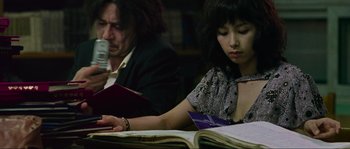 Movie still from “Oldboy” (2003), directed by Park Chan-wook – A woman sitting at a table reading a book; Medium shot, High angle