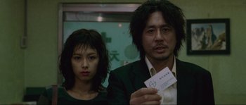 Movie still from “Oldboy” (2003), directed by Park Chan-wook – A man and a woman standing next to each other holding papers; Close Up shot, Low angle