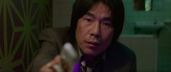 Movie still from “Oldboy” (2003), directed by Park Chan-wook – A man in a suit and tie holding a remote control; Close Up shot, Low angle