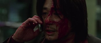 Movie still from “Oldboy” (2003), directed by Park Chan-wook – A man with blood all over his face talking on a cell phone; Close Up shot, High angle
