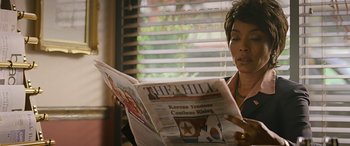 Movie still from “Olympus Has Fallen” (2013), directed by Antoine Fuqua – A woman sitting down reading a newspaper; Close Up shot, Over the shoulder angle