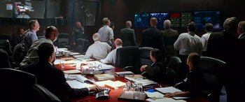 Movie still from “Olympus Has Fallen” (2013), directed by Antoine Fuqua – A group of people sitting at a table in front of a tv; Wide shot, Over the shoulder angle
