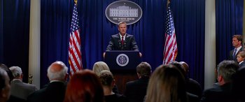 Movie still from “Olympus Has Fallen” (2013), directed by Antoine Fuqua – A man in a suit is speaking at a podium; Medium shot, Over the shoulder angle