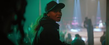 Movie still from “On the Come Up” (2022), directed by Sanaa Lathan – A woman wearing a hat and a black jacket in front of a green background; Close Up shot, Over the shoulder angle
