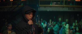 Movie still from “On the Come Up” (2022), directed by Sanaa Lathan – A woman in a black hooded jacket standing in front of a group of people; Medium shot, Over the shoulder angle