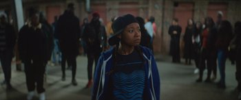 Movie still from “On the Come Up” (2022), directed by Sanaa Lathan – A young woman in a blue jacket and a black hat; Medium shot, Over the shoulder angle