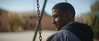 Movie still from “On the Come Up” (2022), directed by Sanaa Lathan – A man sitting on top of a metal swing; Close Up shot, Over the shoulder angle