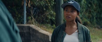 Movie still from “On the Come Up” (2022), directed by Sanaa Lathan – A woman wearing a baseball cap standing in front of a tree; Close Up shot, Over the shoulder angle