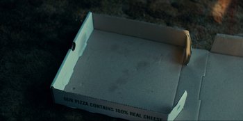 Movie still from “One Day as a Lion” (2023), directed by John Swab – An open pizza box sitting on top of a table; Extreme Close Up shot, High angle
