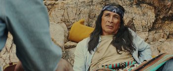 Movie still from “One Ranger” (2023), directed by Jesse V. Johnson – A man sitting on the ground wearing a bandanna; Close Up shot, Over the shoulder angle