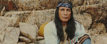 Movie still from “One Ranger” (2023), directed by Jesse V. Johnson – A man with long black hair sitting on the ground; Medium shot, Over the shoulder angle