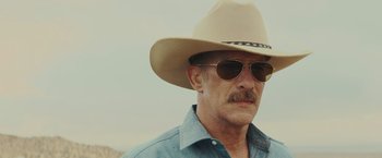 Movie still from “One Ranger” (2023), directed by Jesse V. Johnson – A person wearing sunglasses and a hat; Close Up shot, Low angle