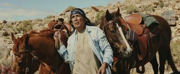 Movie still from “One Ranger” (2023), directed by Jesse V. Johnson – A man standing next to two brown horses on a rocky hillside; Medium shot, Low angle