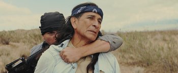 Movie still from “One Ranger” (2023), directed by Jesse V. Johnson – An older man with long black hair and a blue bandanna on his head; Close Up shot, Over the shoulder angle