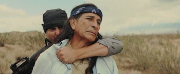 Movie still from “One Ranger” (2023), directed by Jesse V. Johnson – An older man with long black hair is holding a younger man's shoulder; Close Up shot, Over the shoulder angle