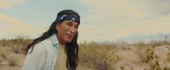 Movie still from “One Ranger” (2023), directed by Jesse V. Johnson – A man with long black hair wearing a bandana; Medium shot, Over the shoulder angle