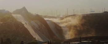 Movie still from “One Ranger” (2023), directed by Jesse V. Johnson – A view of a dirt road and a hill with smoke coming out of it; Extreme Wide shot, Low angle
