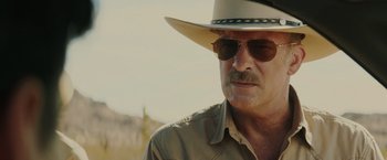 Movie still from “One Ranger” (2023), directed by Jesse V. Johnson – A person wearing sunglasses and a hat; Close Up shot, Over the shoulder angle