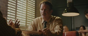 Movie still from “One Ranger” (2023), directed by Jesse V. Johnson – A man sitting at a table reading a newspaper; Close Up shot, Over the shoulder angle