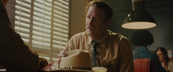 Movie still from “One Ranger” (2023), directed by Jesse V. Johnson – A man sitting at a table wearing a hat; Close Up shot, Over the shoulder angle