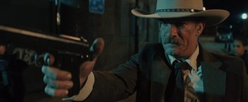 Movie still from “One Ranger” (2023), directed by Jesse V. Johnson – A man in a suit and a cowboy hat holding a gun; Close Up shot, Low angle
