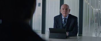 Movie still from “One Ranger” (2023), directed by Jesse V. Johnson – An older man sitting at a table with a laptop; Medium shot, Over the shoulder angle