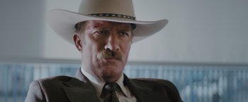 Movie still from “One Ranger” (2023), directed by Jesse V. Johnson – A person wearing a suit and a cowboy hat; Close Up shot, Low angle