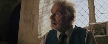 Movie still from “One Ranger” (2023), directed by Jesse V. Johnson – An older man wearing a vest and a tie; Close Up shot, Over the shoulder angle