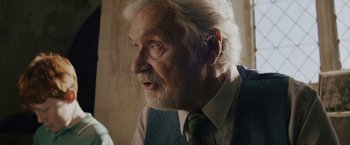 Movie still from “One Ranger” (2023), directed by Jesse V. Johnson – An old man with a beard and a green neck tie; Close Up shot, Over the shoulder angle