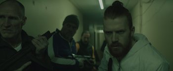 Movie still from “One Ranger” (2023), directed by Jesse V. Johnson – A group of men standing next to each other in a room; Medium shot, Over the shoulder angle