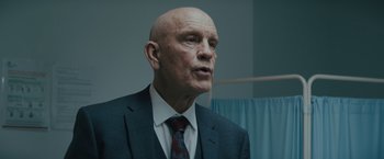 Movie still from “One Ranger” (2023), directed by Jesse V. Johnson – A man in a suit and tie in front of a hospital bed; Close Up shot, Low angle