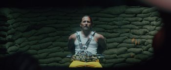 Movie still from “One Ranger” (2023), directed by Jesse V. Johnson – A man in chains sitting in front of a brick wall; Medium shot, High angle