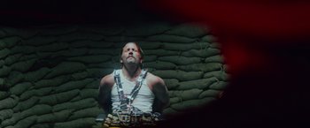 Movie still from “One Ranger” (2023), directed by Jesse V. Johnson – A man wearing chains is sitting in front of a brick wall; Medium shot, High angle