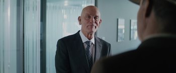 Movie still from “One Ranger” (2023), directed by Jesse V. Johnson – An older man wearing a suit and tie; Close Up shot, Over the shoulder angle