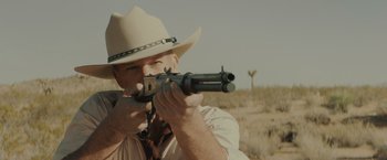 Movie still from “One Ranger” (2023), directed by Jesse V. Johnson – A man wearing a cowboy hat is holding a rifle; Close Up shot, Low angle