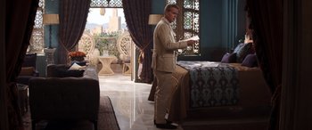 Movie still from “Operation Fortune: Ruse de Guerre” (2023), directed by Guy Ritchie – A man standing in front of a bed in a room; Wide shot, Over the shoulder angle