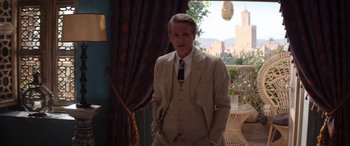 Movie still from “Operation Fortune: Ruse de Guerre” (2023), directed by Guy Ritchie – A man in a suit and tie standing in front of a window; Medium shot, Over the shoulder angle