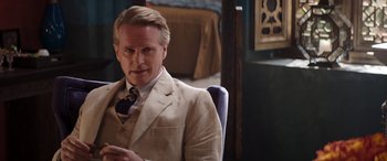 Movie still from “Operation Fortune: Ruse de Guerre” (2023), directed by Guy Ritchie – A man sitting in a chair wearing a suit and tie; Close Up shot, Over the shoulder angle