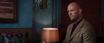 Movie still from “Operation Fortune: Ruse de Guerre” (2023), directed by Guy Ritchie – A man in a suit and tie holding a lamp in a room; Medium shot, Low angle