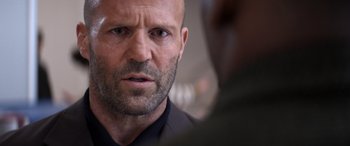 Movie still from “Operation Fortune: Ruse de Guerre” (2023), directed by Guy Ritchie – A person wearing a suit and tie; Close Up shot, Over the shoulder angle