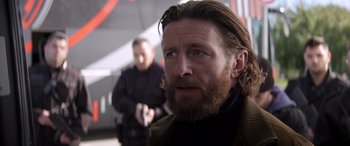 Movie still from “Operation Fortune: Ruse de Guerre” (2023), directed by Guy Ritchie – A person with long hair and a beard; Close Up shot, Over the shoulder angle