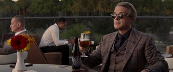 Movie still from “Operation Fortune: Ruse de Guerre” (2023), directed by Guy Ritchie – A man sitting at a table holding a glass of beer; Medium shot, Over the shoulder angle