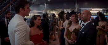 Movie still from “Operation Fortune: Ruse de Guerre” (2023), directed by Guy Ritchie – A group of people standing in a room with drinks; Medium shot, Over the shoulder angle