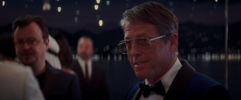 Movie still from “Operation Fortune: Ruse de Guerre” (2023), directed by Guy Ritchie – A person wearing a suit and glasses; Close Up shot, Over the shoulder angle