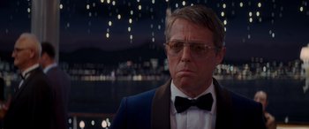 Movie still from “Operation Fortune: Ruse de Guerre” (2023), directed by Guy Ritchie – A person wearing glasses and a bow tie; Close Up shot, Over the shoulder angle