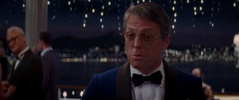 Movie still from “Operation Fortune: Ruse de Guerre” (2023), directed by Guy Ritchie – A person wearing glasses and a bow tie; Close Up shot, Over the shoulder angle