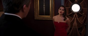 Movie still from “Operation Fortune: Ruse de Guerre” (2023), directed by Guy Ritchie – A woman in a strapless red dress standing in front of a painting; Medium shot, Over the shoulder angle