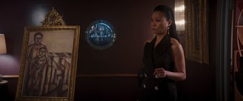 Movie still from “Operation Fortune: Ruse de Guerre” (2023), directed by Guy Ritchie – A woman standing in front of a mirror in front of a painting; Medium shot, Over the shoulder angle